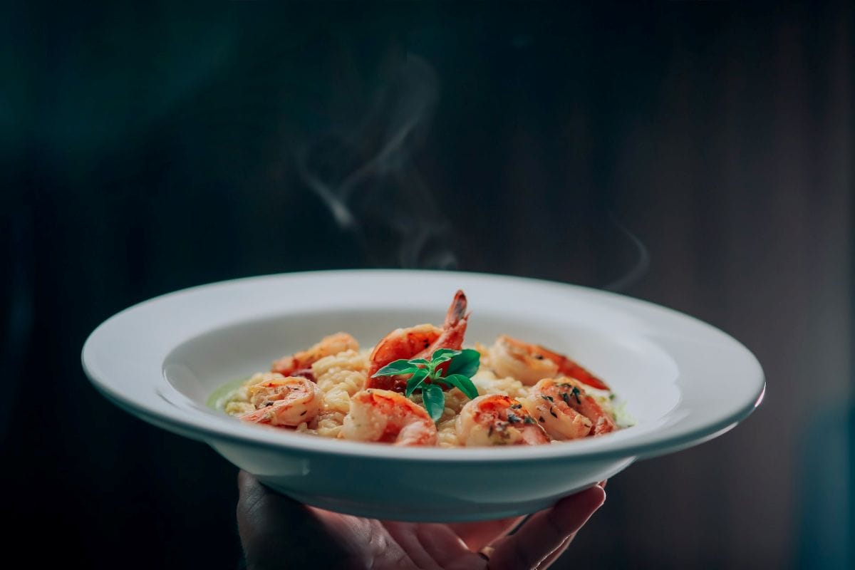 A person holding a ceramic plate with shrimp risotto. 