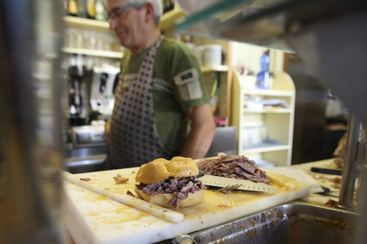 man standing behind deli counter with sandwich on a cutting board