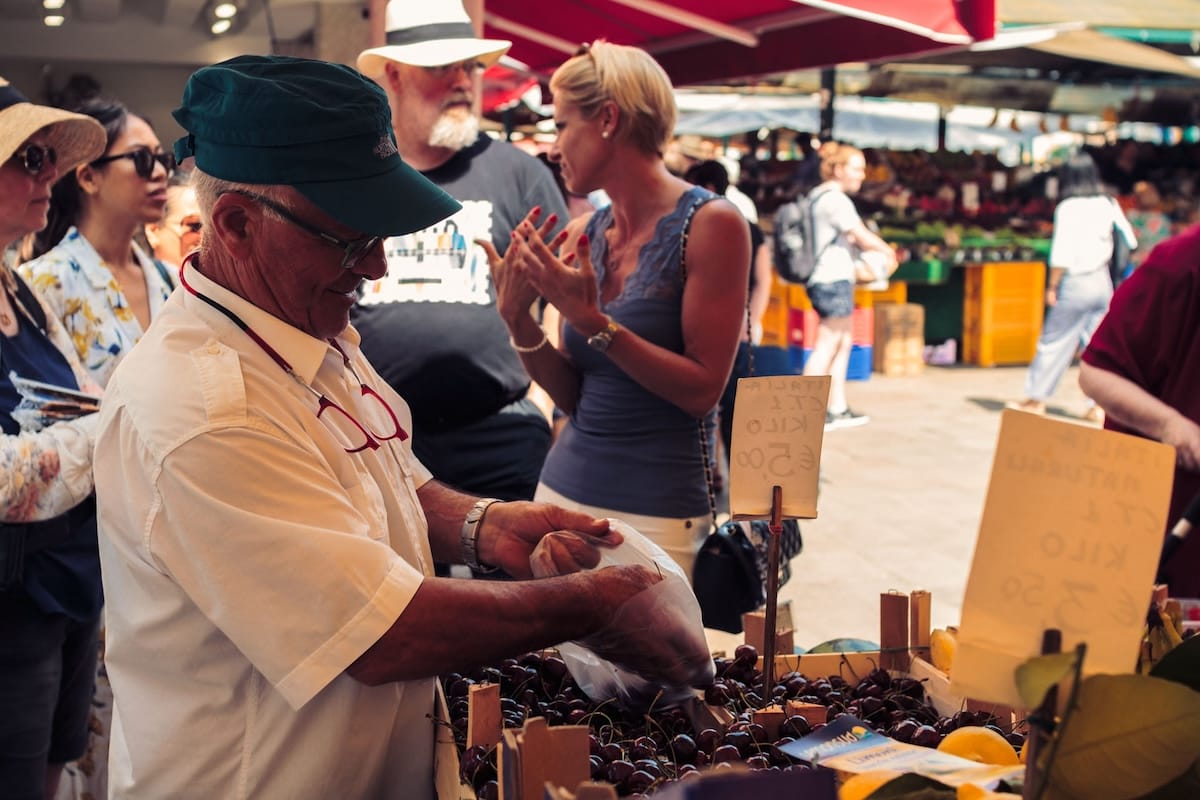 man filling bag with cherries at open-air market