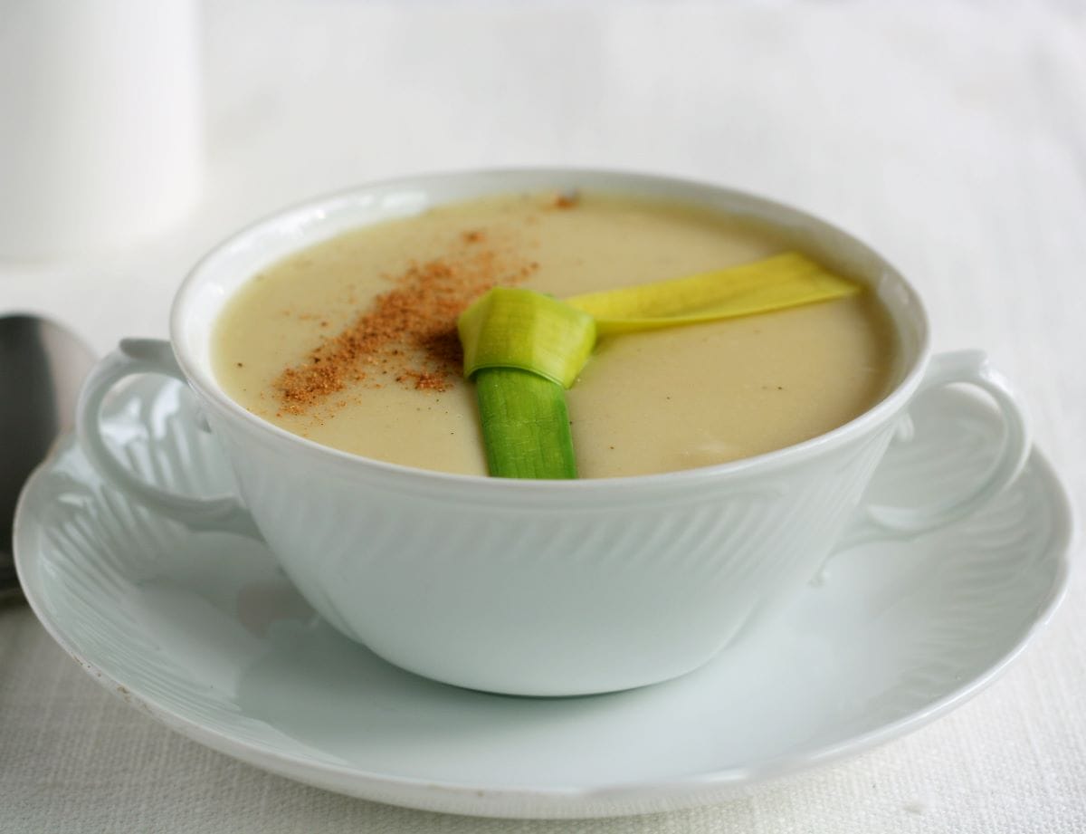 White bowl of creamy soup topped with leeks