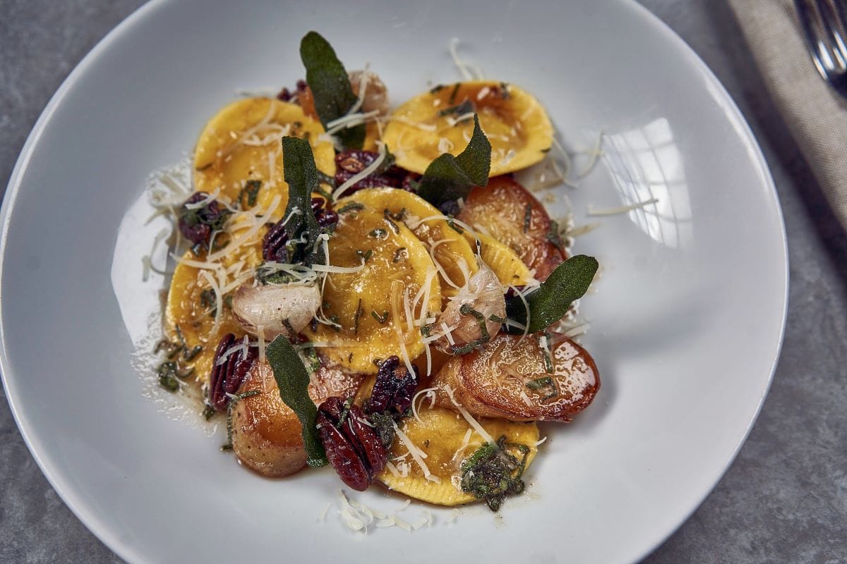 plate of pumpkin raviolis topped with sage, pecans, and cheese.