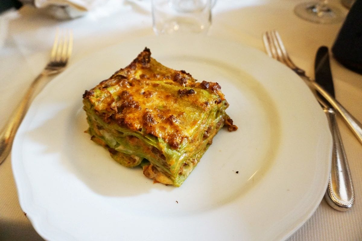 a white plate with green lasagna. 