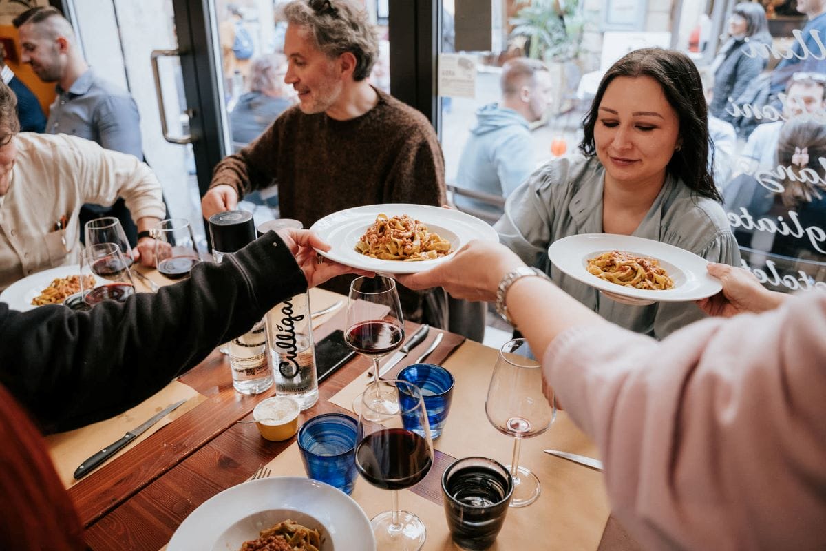 woman passing around plates of pasta to people at a table