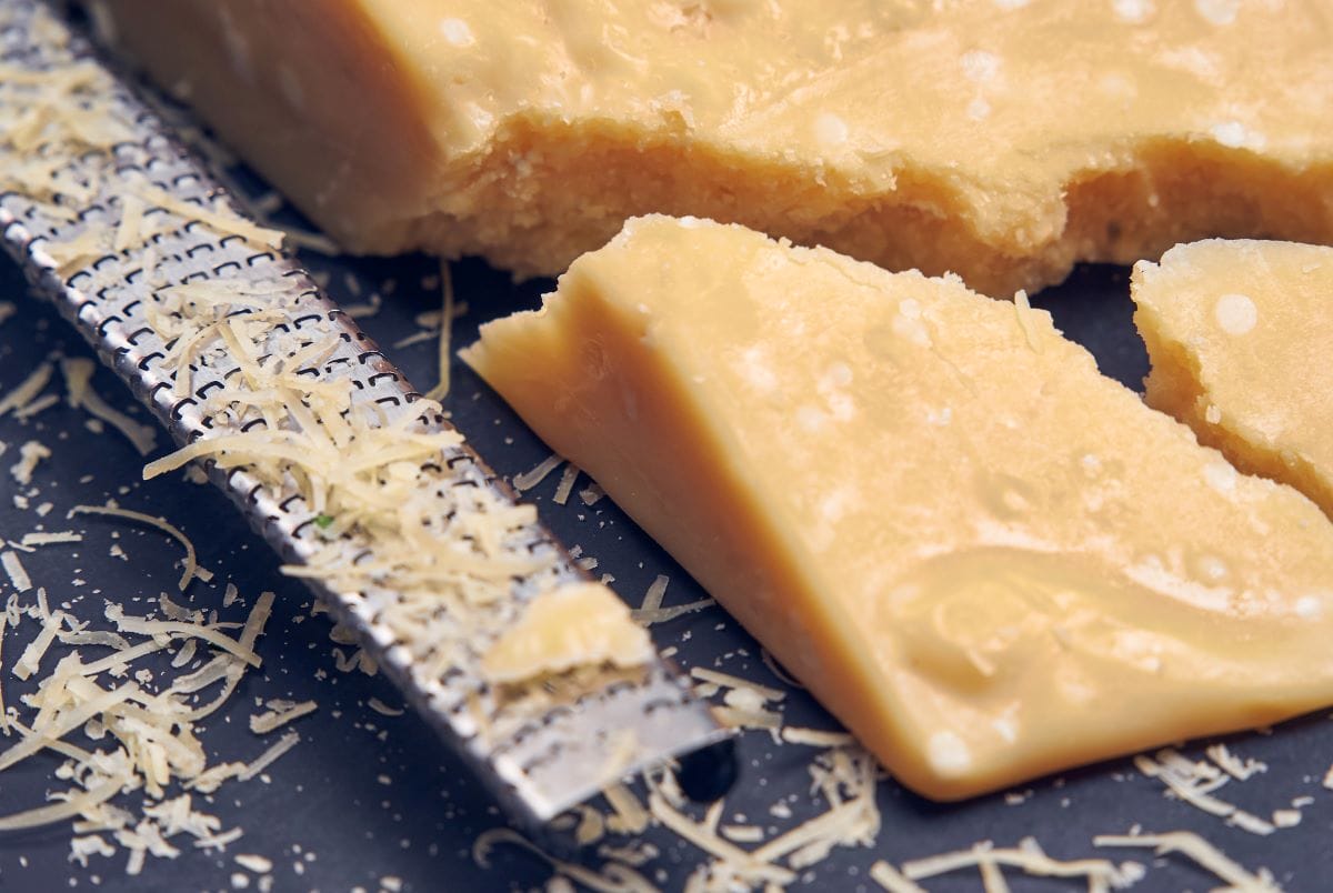 Parmesan on a board next to a cheese grater 