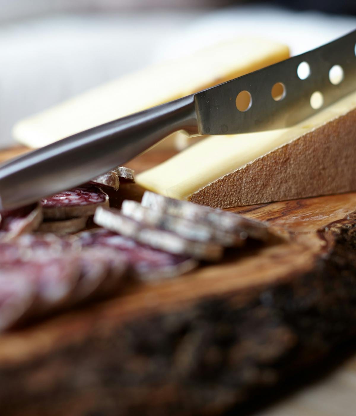 A knife in a wedge of Parmesan and cured meat on a wooden board. 