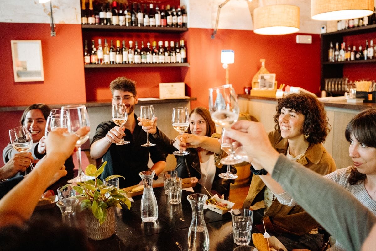 A group of people cheering glasses of white wine at a restaurant in Italy.