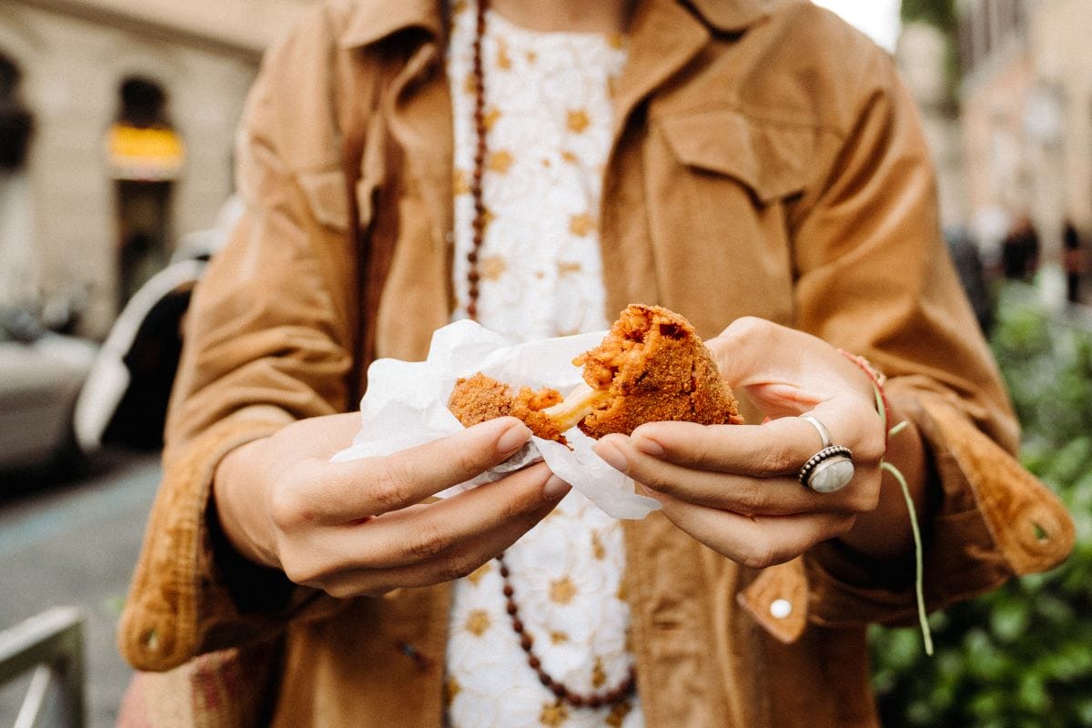 A woman breaking apart a cheesy fried rice ball in Rome, Italy.