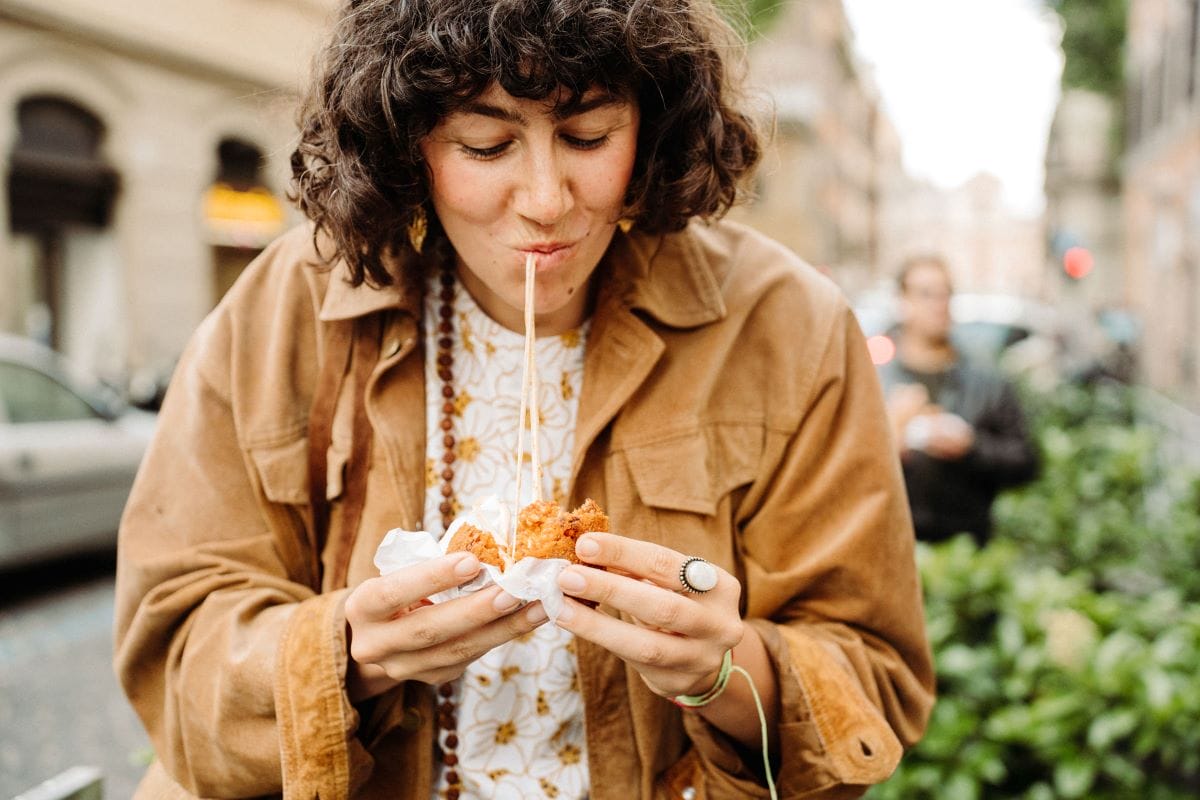 A woman taking a bite out of a fried rice ball in Rome, Italy.