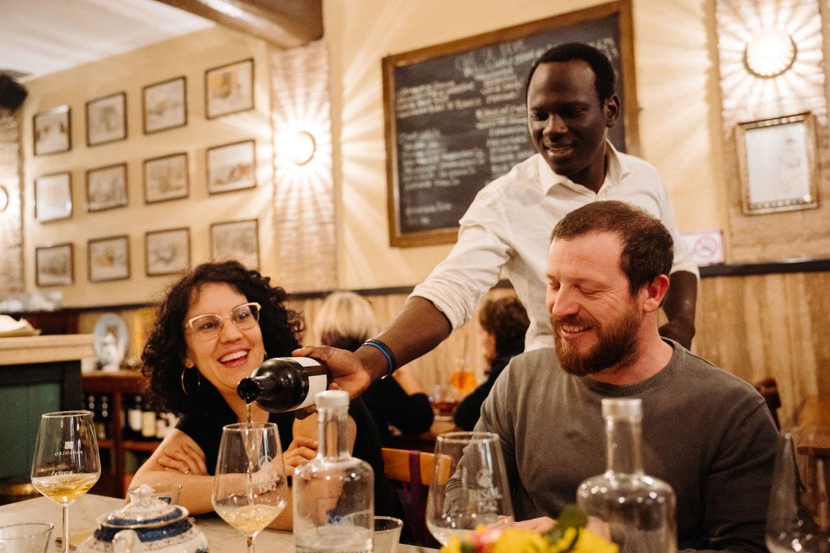 A waiter pouring a glass of Italian wine for two customers.