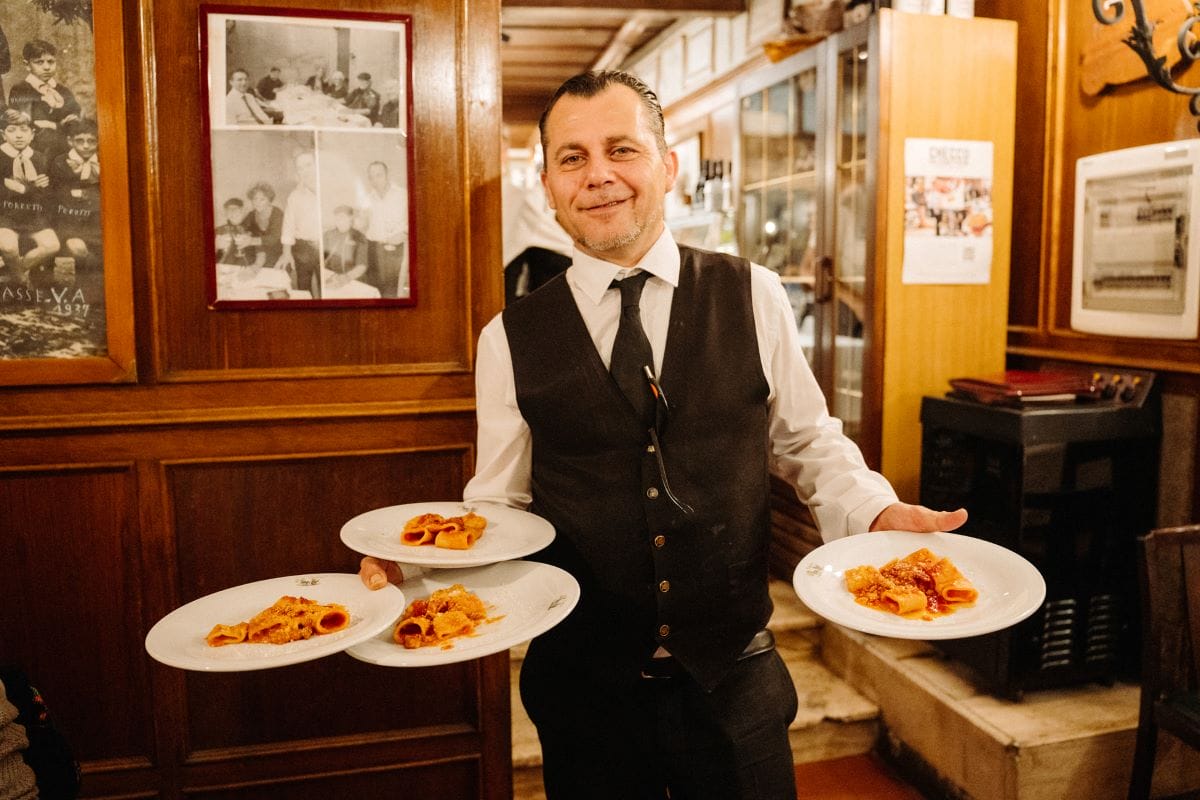 A waiter holding plates of pasta in red sauce.