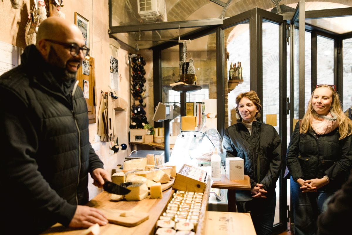 A shop owner explaining different types of Tuscan cheese to clients.