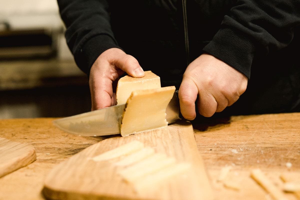 A shop owner slicing Italian cheese on a wooden board.