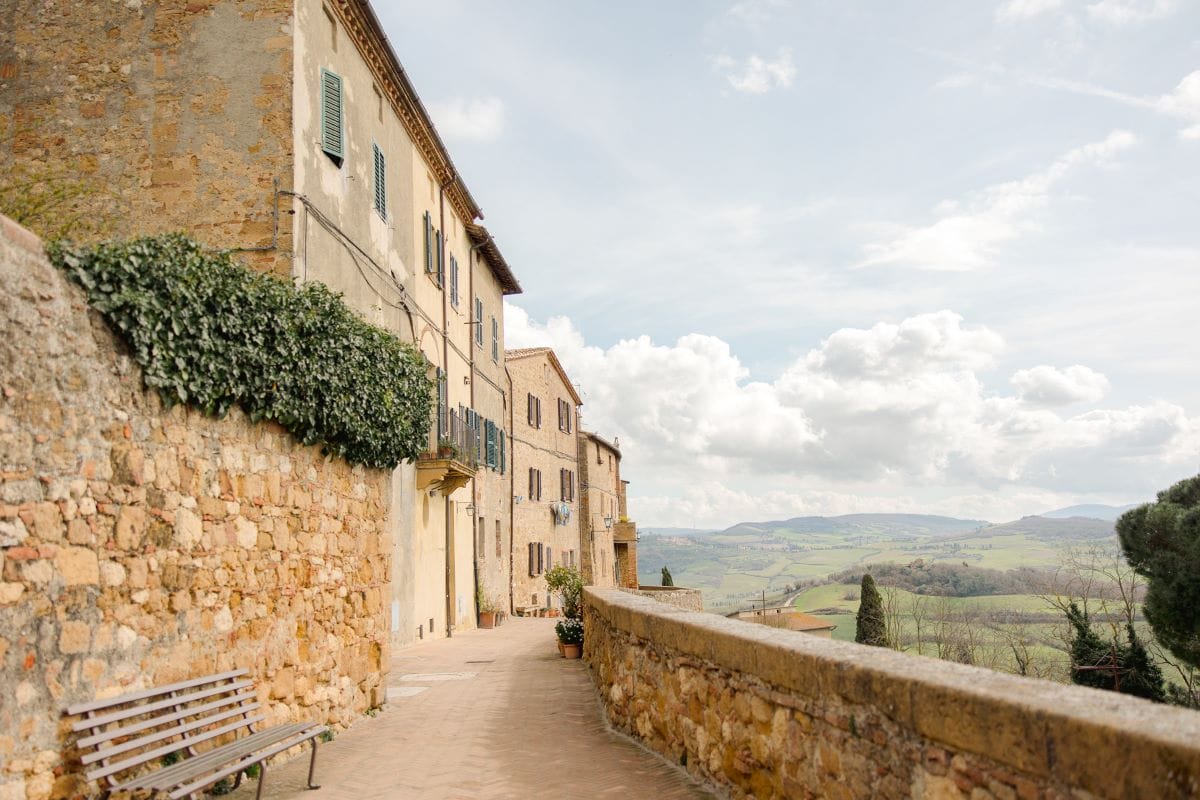 A cobblestone path with stone houses on the left, leading to views of the mountain sides in a small village in Tuscany.