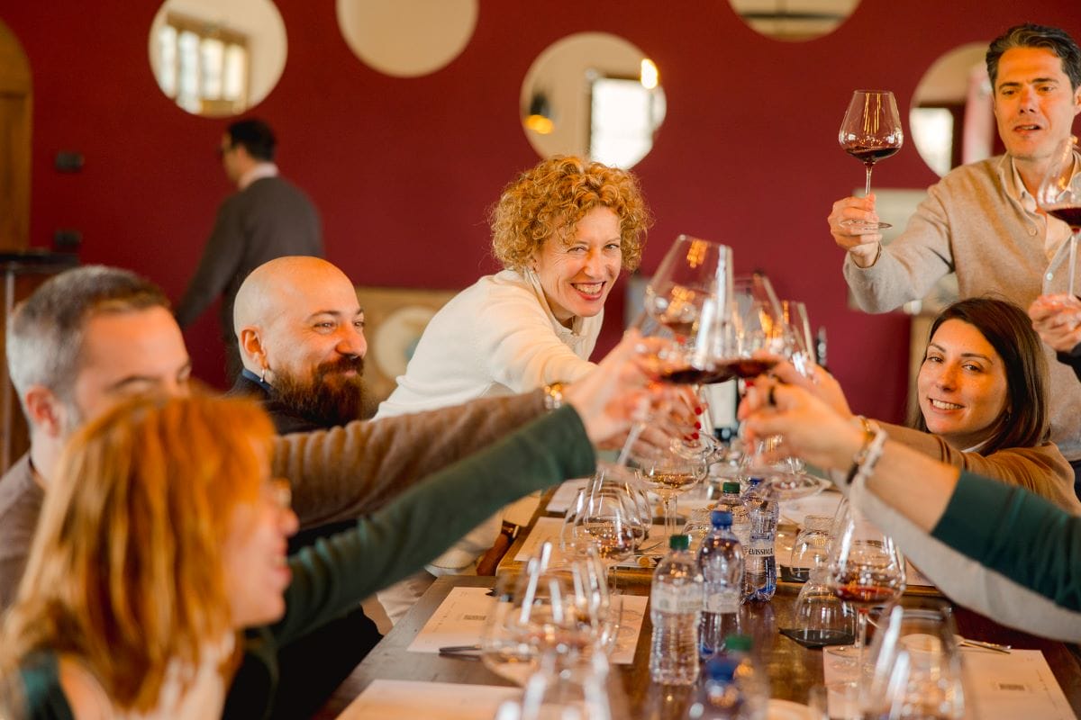 A group of people cheering wine glasses at a long dining table.