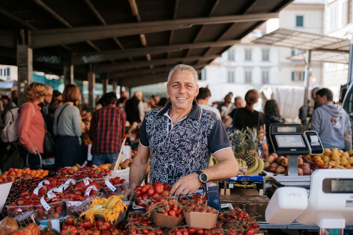 man standing over a selection of tomatoes in a food market