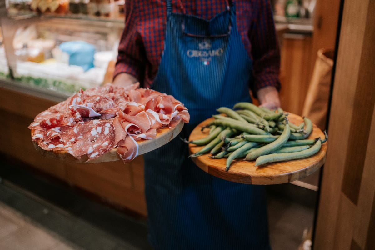 a person holding two round cutting boards topped with charcuterie and beans