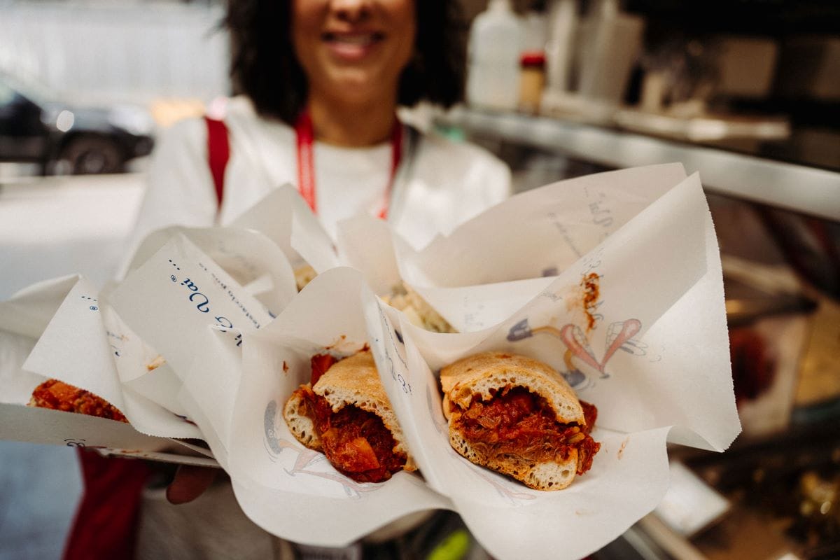 woman holding many small sandwiches wrapped in butcher paper