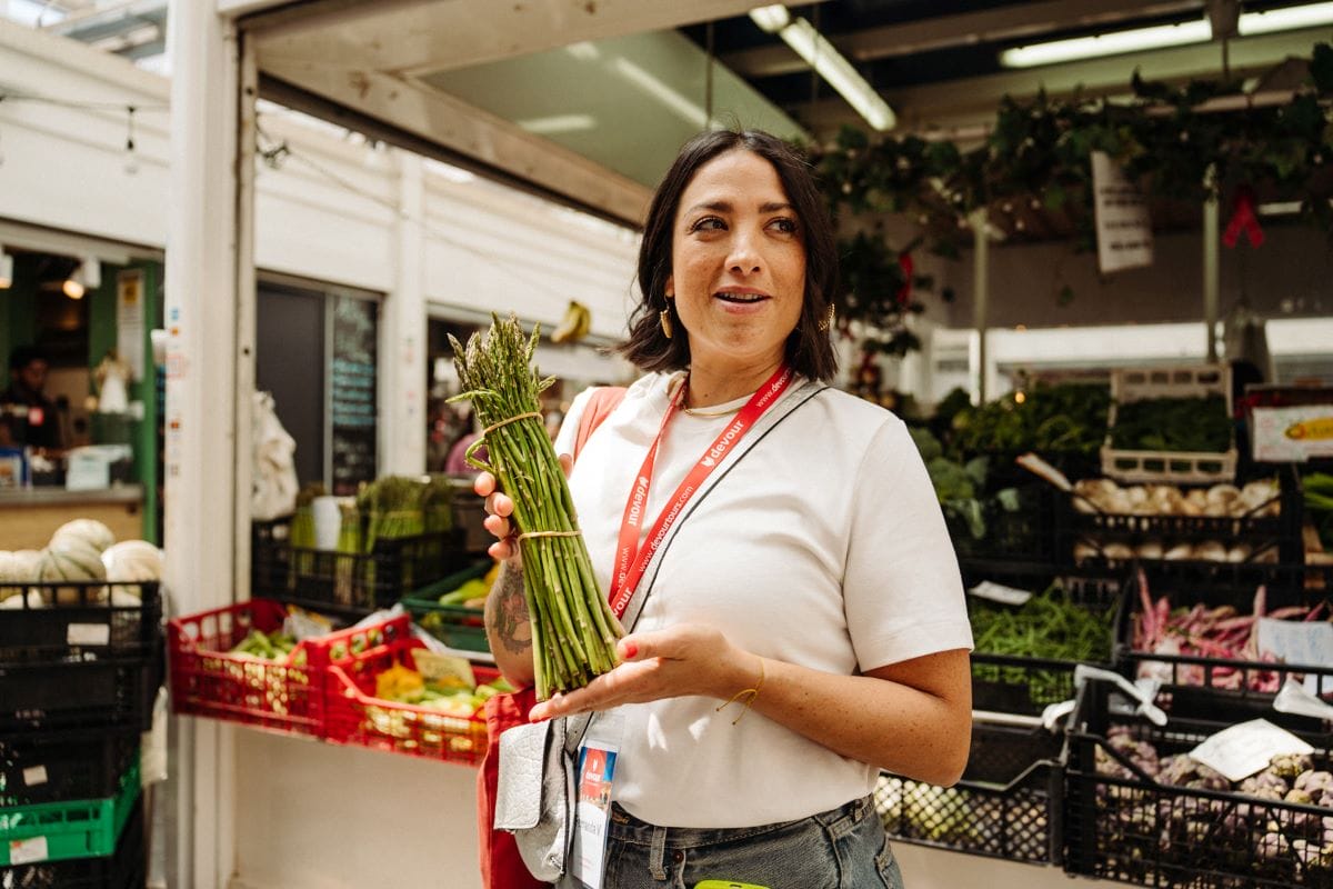 a woman holding a bunch of asparagus in a food market