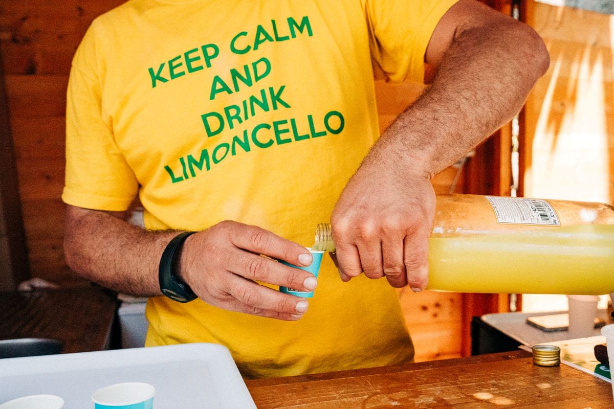 man in yellow shirt pouring yellow liquid into a small blue cup