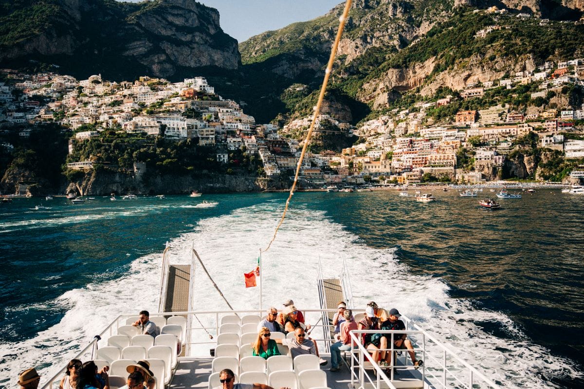 people on a boat with a beautiful view of colorful houses built on a cliffside overlooking the sea